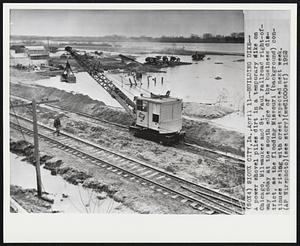 Building Dike- A power shovel piles dirt in a temporary like on Chicago, Milwaukee and St. Paul railroad right-of-way today at the south edge of the business district, as the flooding Missouri (background) continuee rising with crest expected next week.