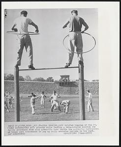 Hula Hooping,Hard Way-Two inmates of the St. Cloud Reformatory defy gravity while leading a hula-hooping session for fellow prisoners from atop gymnastics bars inside the walls.The vari-colored hoops were introduced to pep up daily exercise periods in the yard.