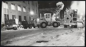 Out to Sea goes white stuff piled high in Copley Sq., as snow melter accepts load and then ejects it into sewer at right.