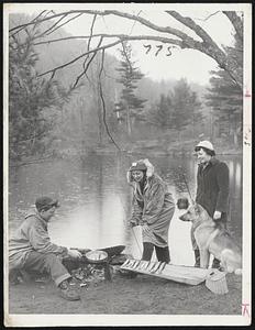 From The Frying Pan – Into The Fishermen. Trout hot off the frying pan is provided by Supt. Herbert Hayner for lucky anglers Barbara Lyman (in parka) and Mrs. Connie Johnson at the Belknap Recreation Area, Laconia-Gilford, N.H. Park officials offered to cook fresh-caught trout on the spot. Despite the usual opening-day rain good catches were reported. “Major” the German shepherd appears to be waiting for a snack too.