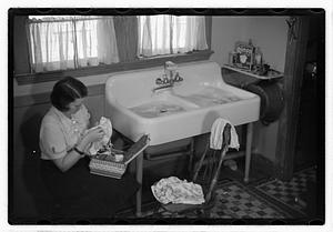 A woman sewing next to a sink full of laundry