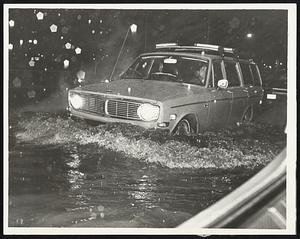 Some Boston streets became waterways yesterday as water reached hub cap depth. Here, motorist plows his way along Charles street opposite Boston Common.