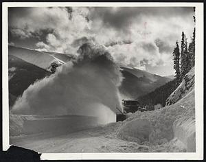 Clearing a Path Through Colorado -- Tons of snow roared down this mountain-side, as government rotary snow plow sought to keep two-mile Berthoud Pass clear for travelers. Note the sun shining through the veil spur by the huge rotary.