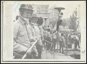 Down with Flag-- As long line of riot-equipment Madison, Wis., police guard city-county building as another officer pulls down red flag placed on pole marching University of Wisconsin students (background) today. Students are continuing their anti-police demonstration for third day. State capitol building is in background.