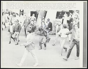 Plainclothes policeman(foreground)strides quickly away from group of jeering dissident students at San Francisco State College 11/21 after he & several other plainclothesmen seized several demonstrators who attempted to close the school for the second time this month. Hundreds of the students marched through buildings and police units were called onto the campus to restore order.
