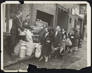 Women's Bread Line In New York City. Although there are many bread lines for men in New York City, similar ones for women had not been organized until recently. The photograph shows the Rev. John H. Evans of the New Hope Mission as he passed out food to women who have a family and can cook at home. On the right is Daniel Platt, chairman of the non-sectarian relief board of the east side. This mission is part of a chain of such institutions in Chicago and other cities conducted by the "Free Apostolic Church of Christ". Some of the women here have walked 30 blocks for the food.