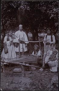 Four women and one man in traditional Greek dress pose by a loom