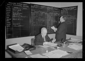 Two office workers with work records on chalkboards
