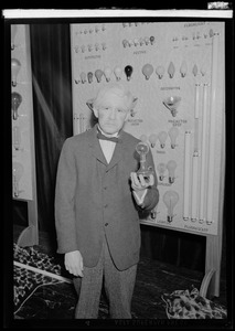 Man dressed as Thomas Edison holding light bulb before light bulb display