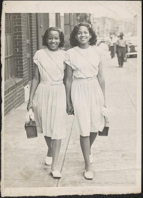 Two young women walk down a sidewalk