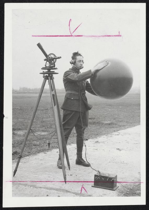 Post-World War I military weatherman prepares to release balloon to probe atmosphere for wind information. He tracked flight visually with theodolite that resembles a surveyor's transit. Data then was reported by wire to weather station.