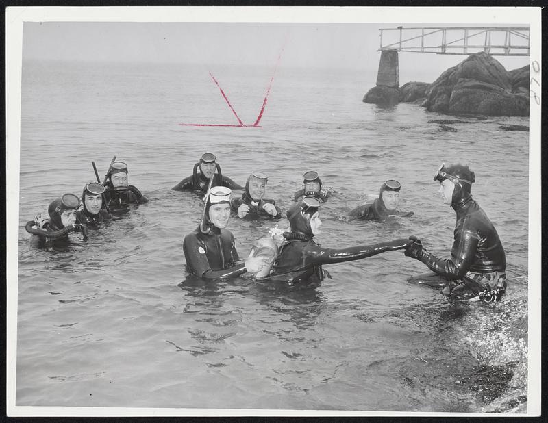 School of Divers - While other skin divers watch, Frank Sanger, president of the New England Divers, helps Mrs. Jane Dainis ashore. Her husband George lifts her air tank. Cold? Not a bit.