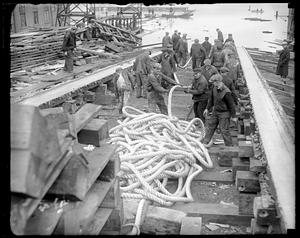 A group of men with a thick rope, possibly at a shipyard
