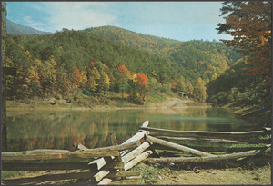 A mountain view taken from behind a rustic fence by a body of water