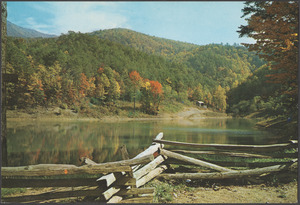 A mountain view taken from behind a rustic fence by a body of water