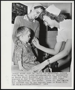 Quizzical-Little Fred Brown, 2, looks apprehensively at thermometer as Nurse Ethel Koechert gets set to take his temperature at Red Cross refugee center last night. Mrs. Byron Brown, the mother, looks on. The family was flooded out of its trailer home in Sioux City.
