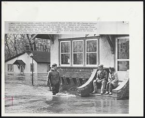 Watching Flood Water Go by--Kenny Holker (left), Monticello, Minn., wades knee-deep in flood waters of Mississippi River at Elk River, Minn., to have talk with Eric Ebner and Mrs. Don Ebner as they sit on steps as flood goes by today. Ebner is an uncle-in-law of Mrs. Ebner, whose home, just down the street, is also surrounded by water.