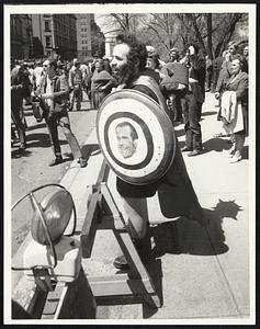 A man stands at a barricade holding a shield painted with a picture of Richard Nixon in the middle of a bullseye