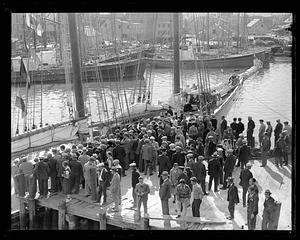A crowd of people in front of a sailing ship