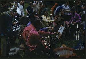 Outdoor group of musicians, some wearing feathered headdresses
