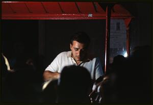 Man under awning in lit area with surrounding figures in shadow