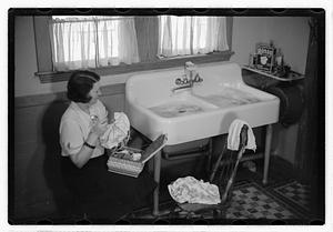 A woman sewing next to a sink full of laundry