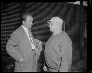 Man in baseball cap and sweatshirt talking with another man