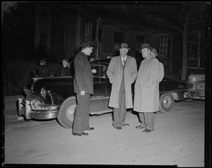 Three men in over coats talk with an officer