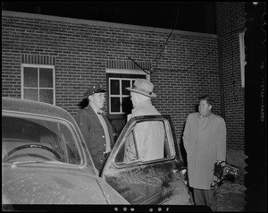Two men talk with an officer next to a car with an open door