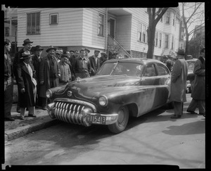 Group gathered around a car, parked on the side of the street