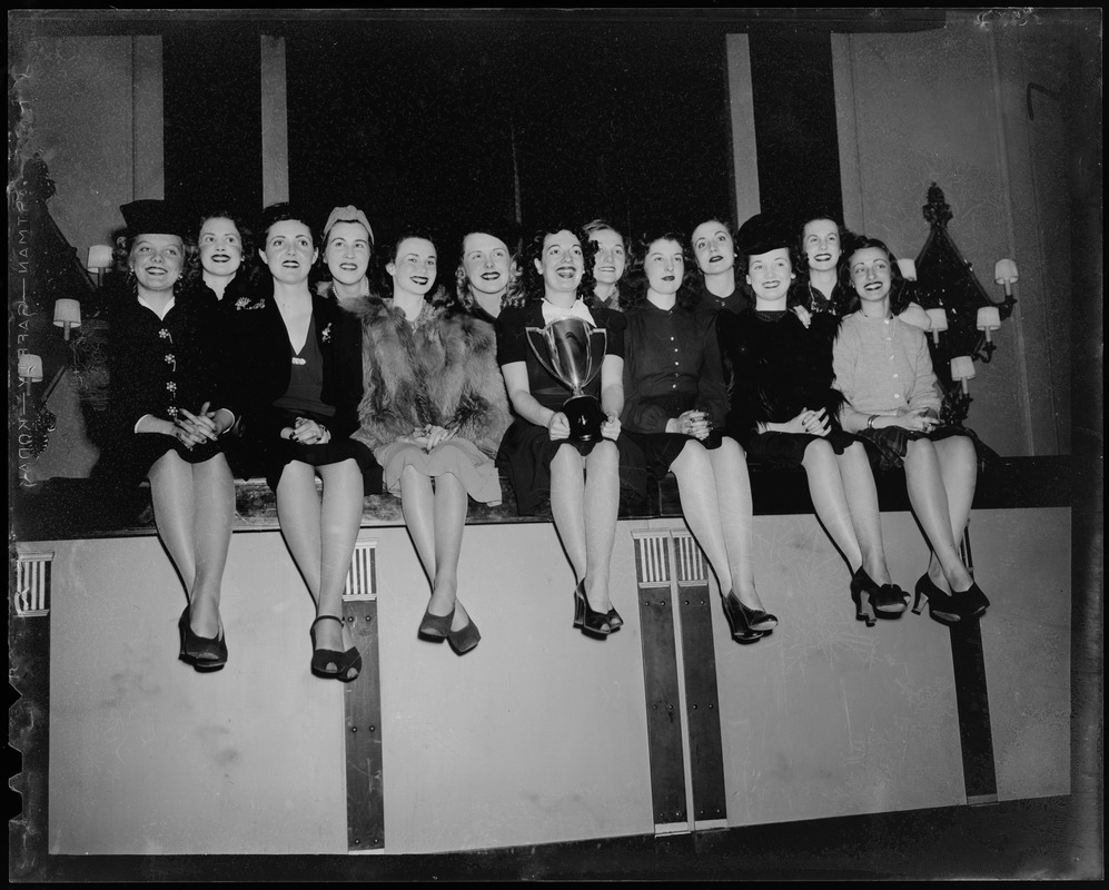 Skaters sitting on a wall, including Sonja Henie holding a trophy