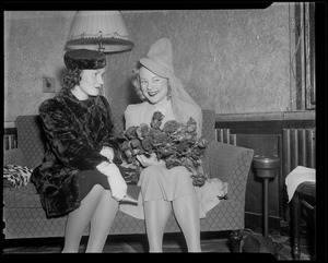 Sonja Henie on the couch with another woman, holding flowers