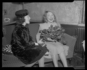 Sonja Henie on the couch with another woman, holding flowers