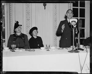 Eddie Cantor at a luncheon or dinner, addressing the room as two women at the table look on