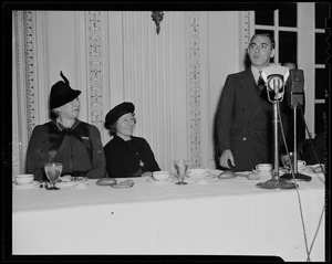 Eddie Cantor at a luncheon or dinner, addressing the room as two women at the table look on