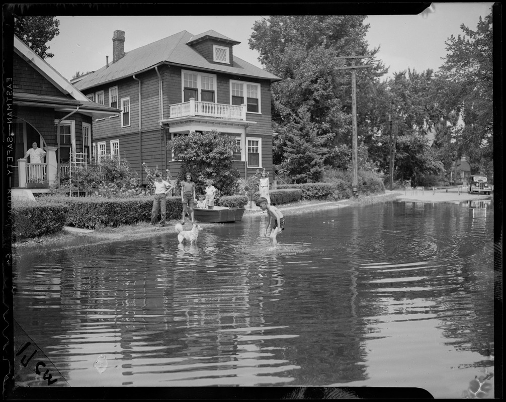 Family in the flooded street by their home, featuring a small child and dog in the water