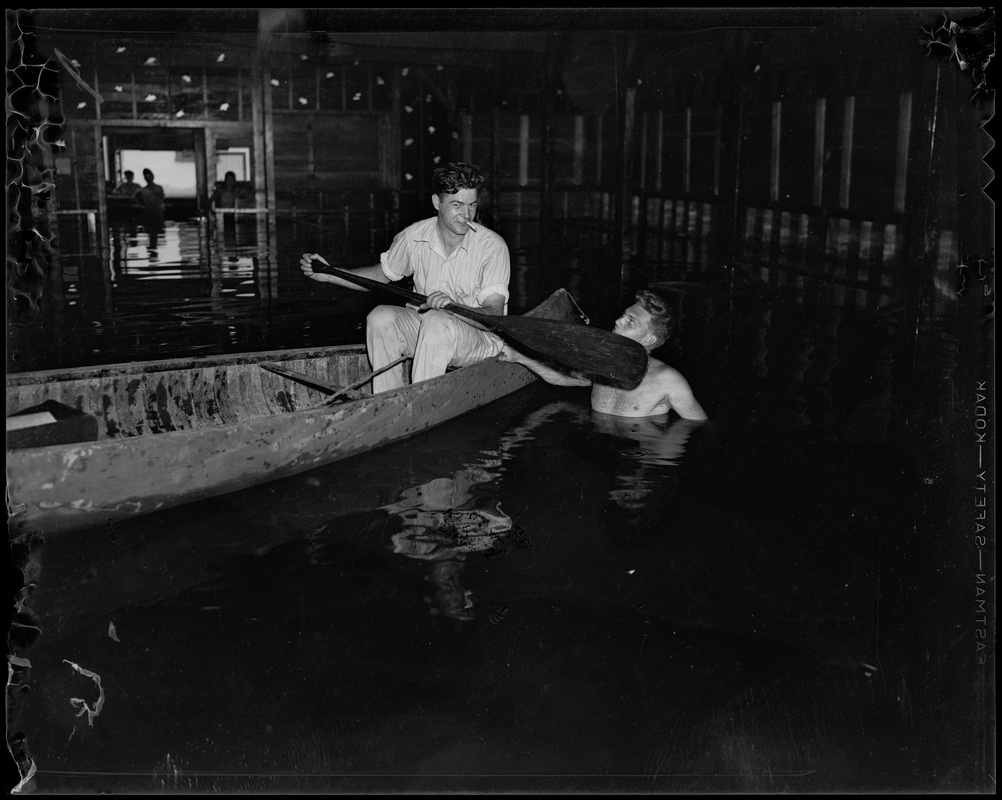 Man in a canoe as another man wades in water next to him