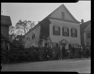Group of people walking in a line by a fallen tree in front of a house