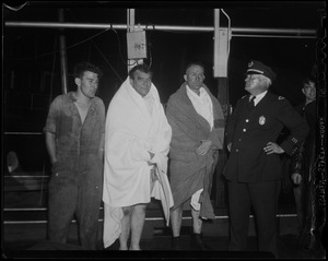 Two men wrapped in blankets, speaking with an officer and a man in coveralls
