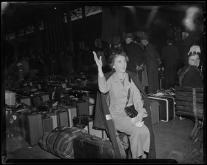 Women seated with luggage behind her, waving