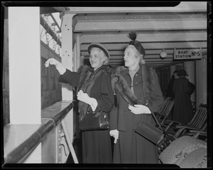 Two women on a ship deck, dressed in hats and furs