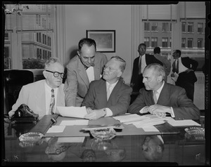 Edward F. Cassell, left, Mayor John B. Hynes, middle, and two other men discussing papers and documents at a desk