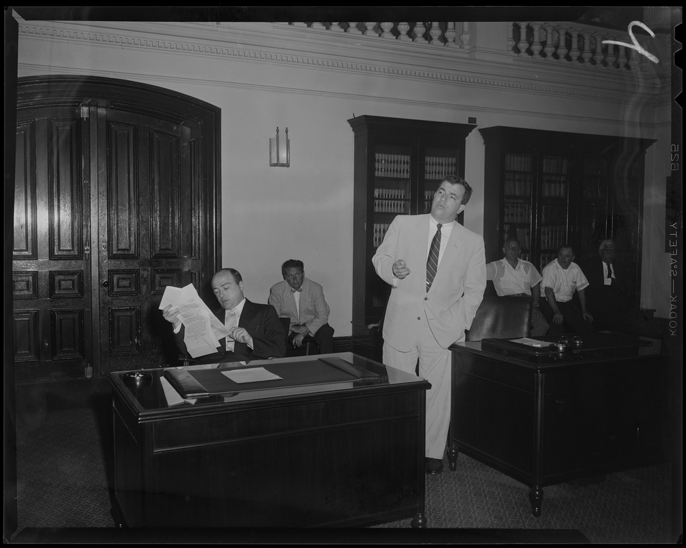 Man sitting at desk reviewing a document while another stands