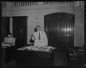 Man standing at desk with newspapers and documents