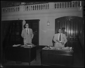 Two men, each at a desk, standing