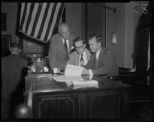 Three men reviewing papers at a desk