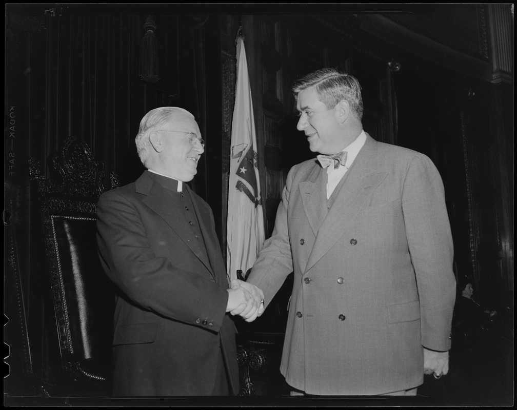 Thomas P. O'Neill shaking hands with a clergyman in front of a flag