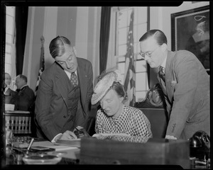 Governor Saltonstall and Prince Bernhard look on while Princess Juliana, seated, signs a book