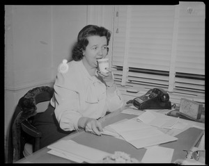 Louise Hicks at desk, sipping from a cup