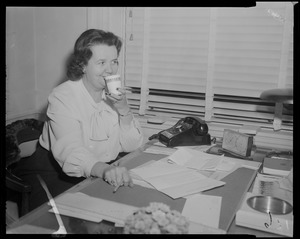 Louise Hicks at desk, sipping from a cup
